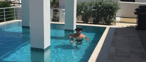 A swimming pool with a person in the water, a white building, and a door with a number.