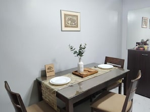 A dining area with a table set for two, a vase with greenery, and a framed picture on the wall. - Manila Airport Budget Stays (Pasay City)