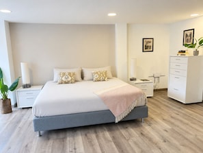 Ein modernes Schlafzimmer mit einem großen Bett, Nachttischen, einer Kommode und einer Topfpflanze.