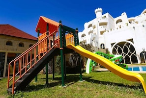 A playground with a slide and stairs, set against a building with white walls and arched windows.
