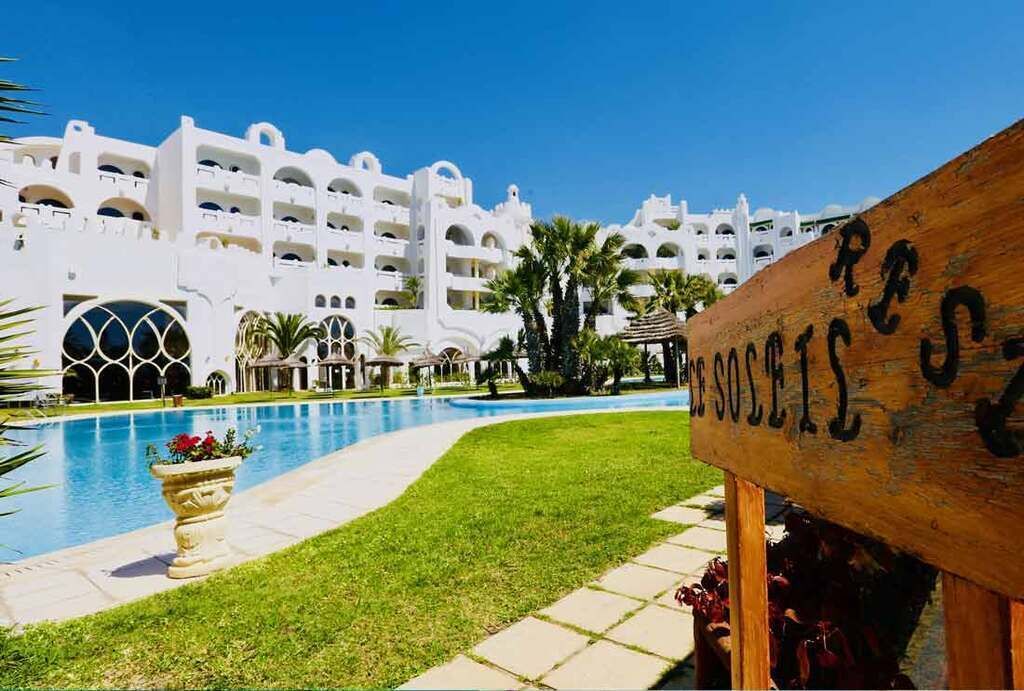 A hotel with a pool, white architecture, and a sign with partially visible text.