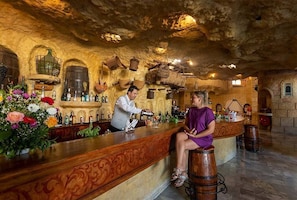 A bar area with a rustic stone ceiling, wooden bar counter, and various bottles and glasses.
