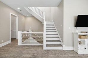 A staircase with a white railing leading to a landing, a flat-screen TV mounted on the wall, and a wooden floor. - Sun Deck | Communal Pool Access (Inlet Beach)
