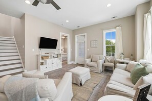 A modern living room with a flat-screen TV, a staircase, and a large window with curtains. - Sun Deck | Communal Pool Access (Inlet Beach)