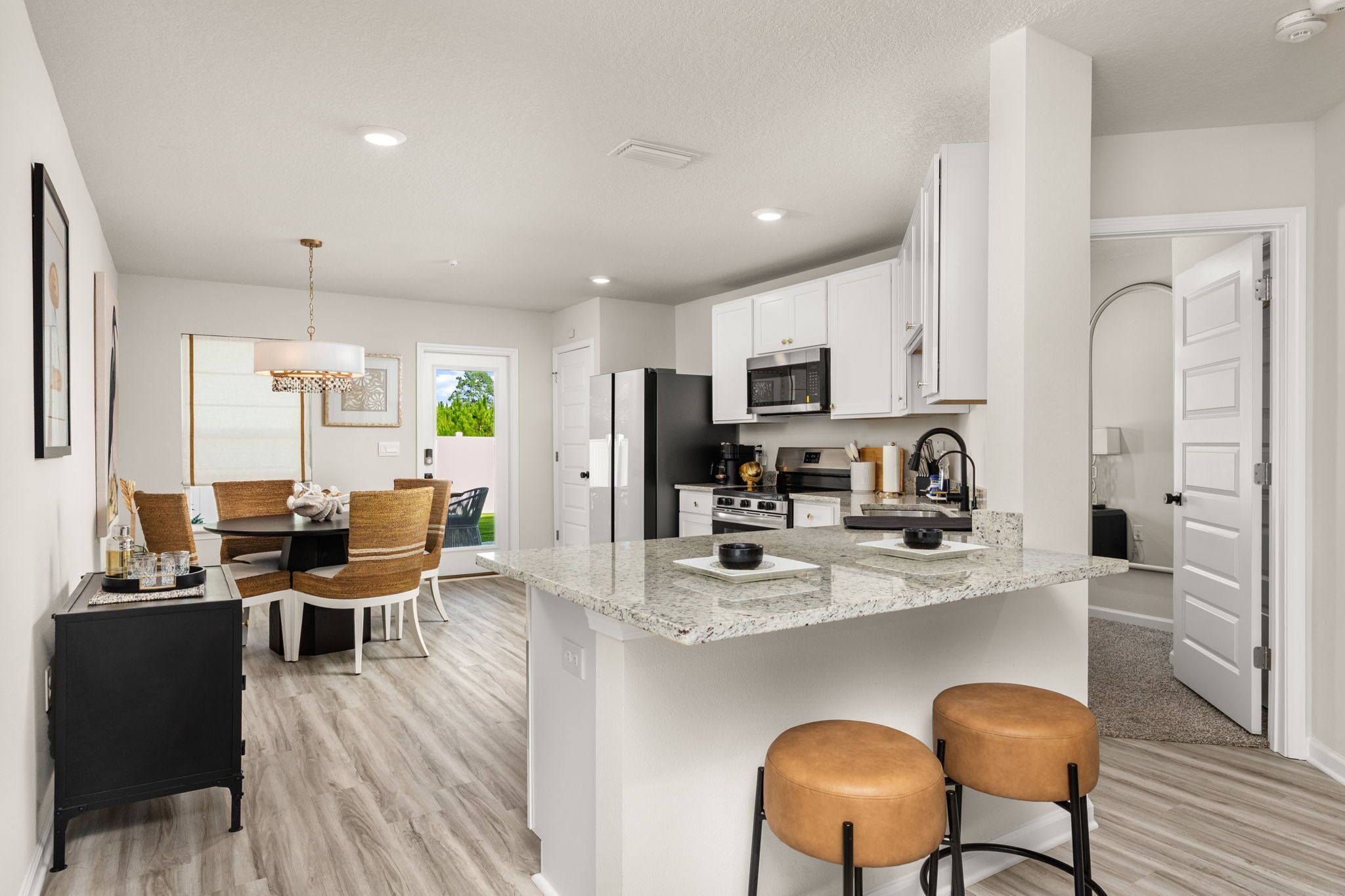 A modern kitchen with a central island, white cabinetry, and a dining area with a chandelier.