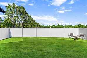 Un jardin avec une clôture blanche, une pelouse bien entretenue et du mobilier d’extérieur.