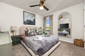 Une chambre à coucher avec un lit, un ventilateur de plafond, une télévision et une fenêtre avec des rideaux.