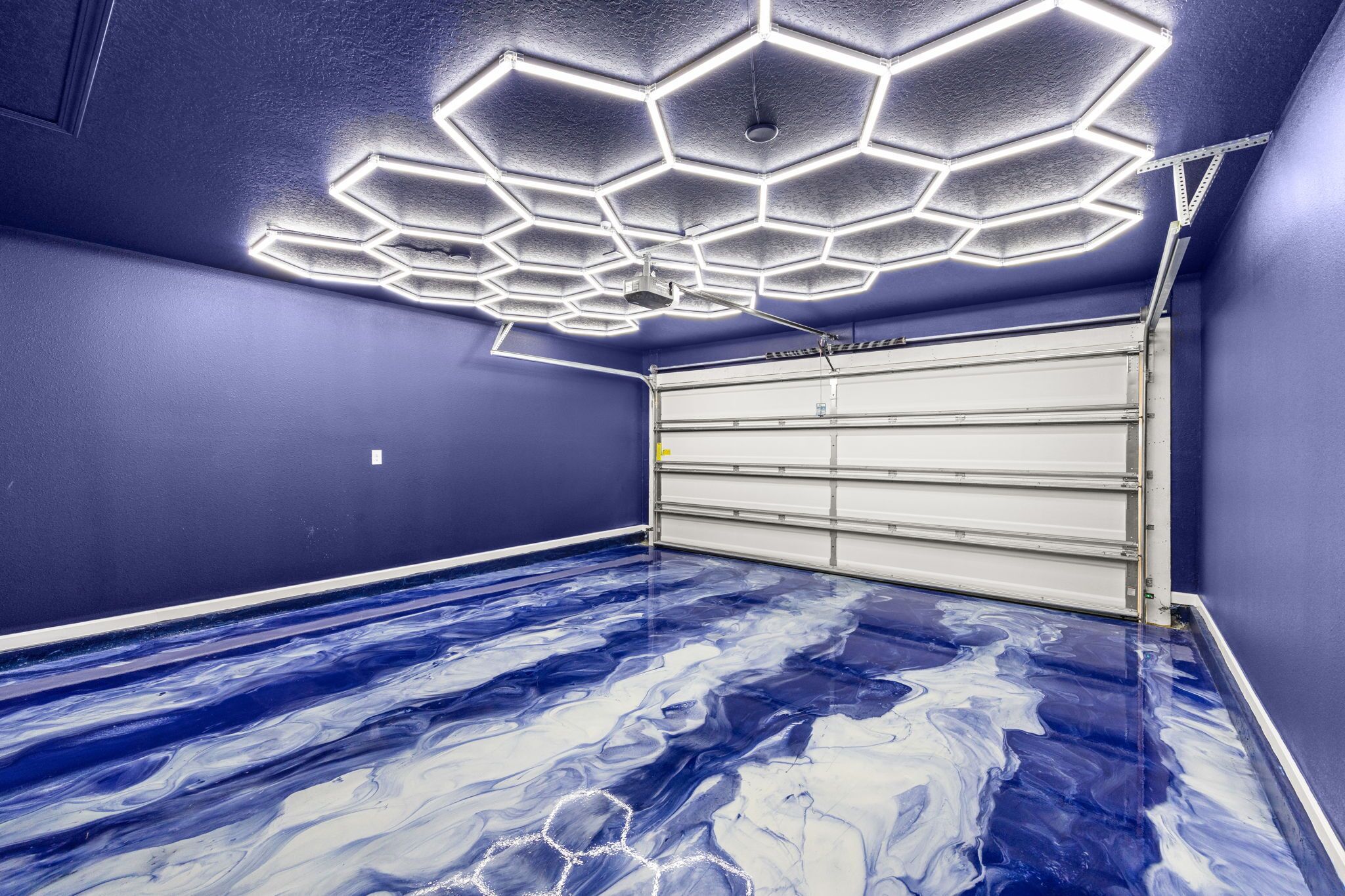 A garage with a blue floor and a ceiling with hexagonal light fixtures.