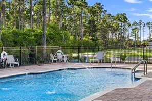 A swimming pool with a water fountain feature, surrounded by a fence and equipped with lounge chairs. - Upscale Coastal Escape | King Suite & Fenced Yard (Port St. Joe)