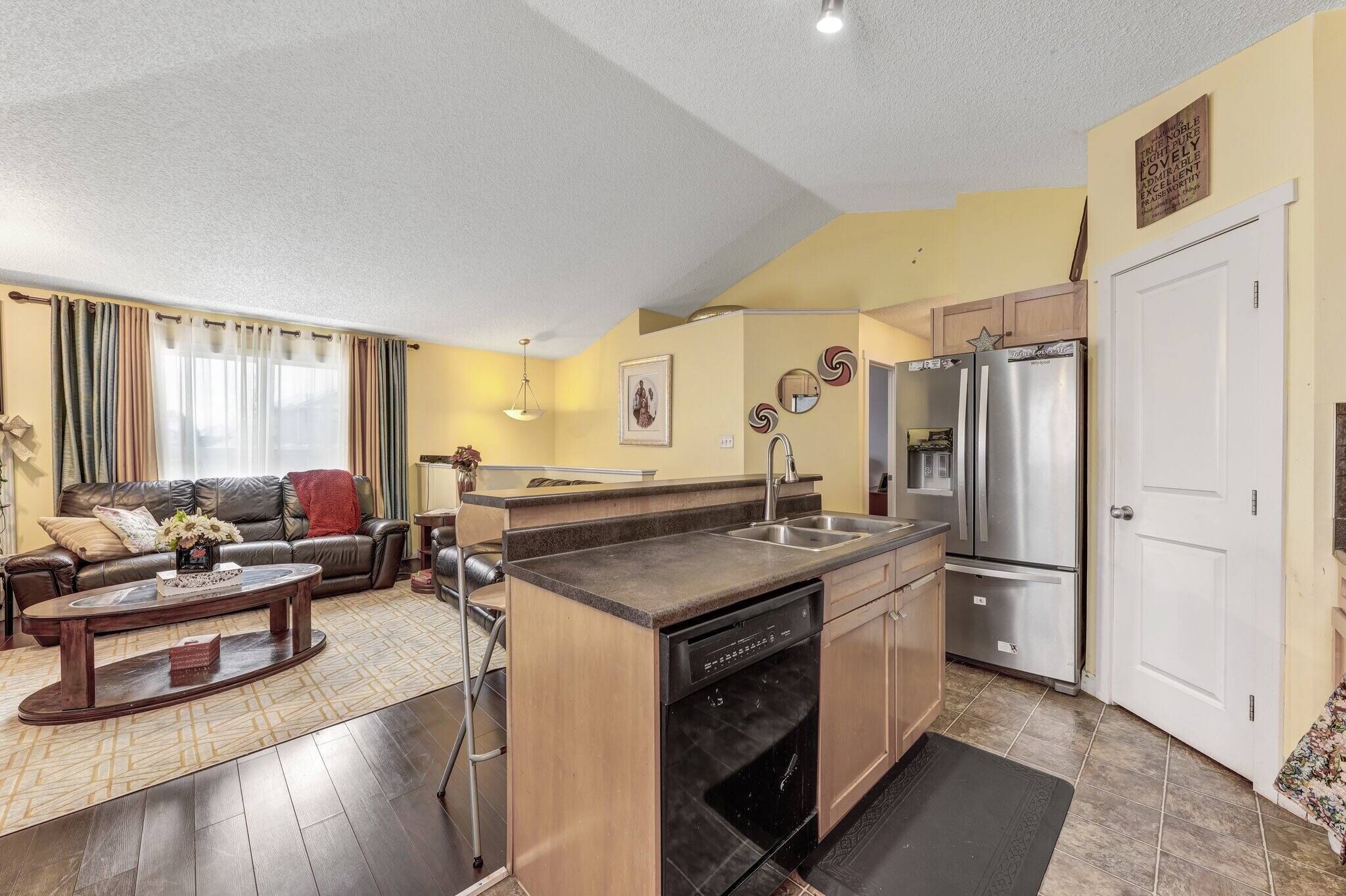 A modern kitchen with a built-in dishwasher, stainless steel refrigerator, and a dining area with a sofa and coffee table.
