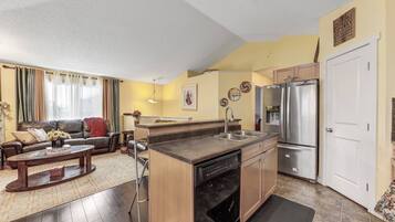 A modern kitchen with a built-in dishwasher, stainless steel refrigerator, and a dining area with a sofa and coffee table.