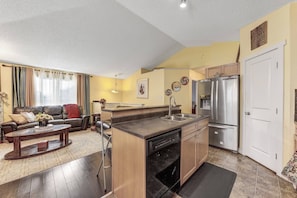Una cocina moderna con lavavajillas integrado, refrigerador de acero inoxidable y un comedor con sofá y mesa de centro.