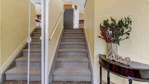 Una escalera conduce a una zona de cocina con una planta decorativa sobre una consola.