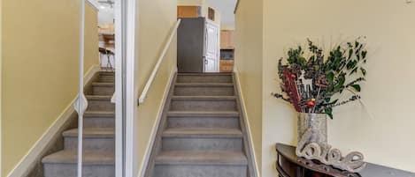 Un escalier menant à un espace cuisine agrémenté d’une plante décorative posée sur une console.