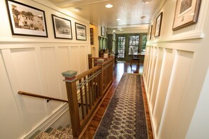 A hallway with wooden flooring, a patterned rug, and framed pictures on the walls.