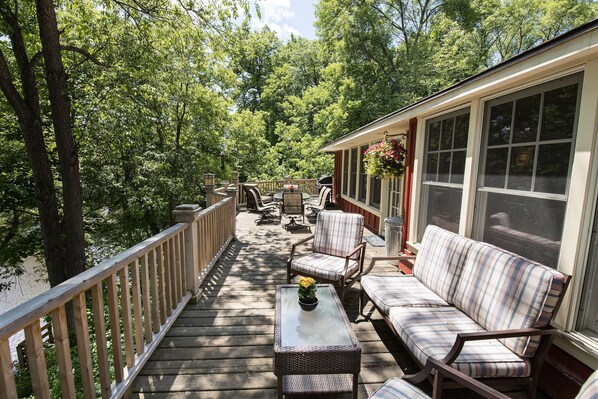 A covered deck with outdoor furniture, a glass-top table, and a hanging flower basket.