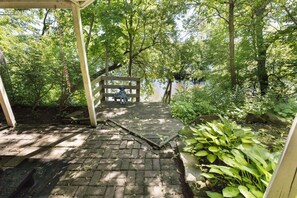 A wooden pathway leading to a bench under a pergola, surrounded by lush greenery and a body of water. - Charming river house in historic Marine on Saint Croix- 2 bedrooms, 3 bathrooms (Marine on Saint Croix)