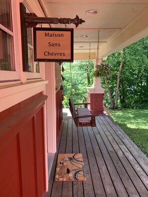 A porch with a swing chair, a hanging sign, and a welcome mat.