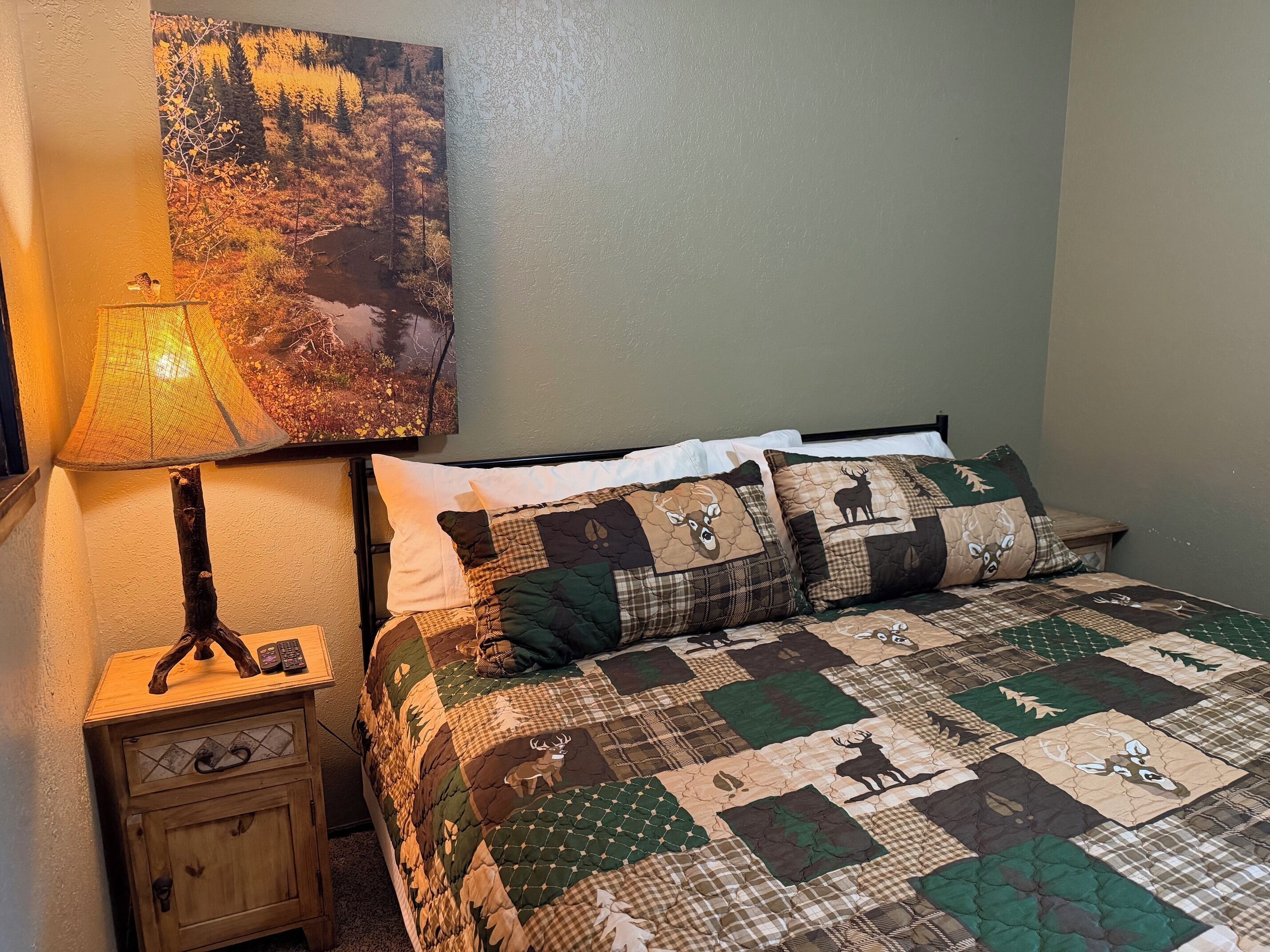 Een slaapkamer met een bed, nachtkastje, lamp en een wanddecoratie.