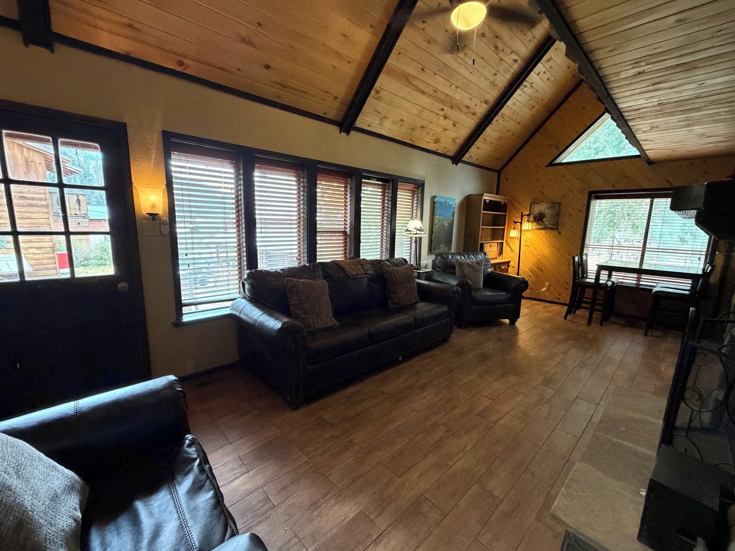 A cozy living room with a wooden ceiling, a leather sofa, a dining table, and a fireplace.
