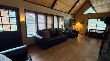 A cozy living room with a wooden ceiling, a leather sofa, a dining table, and a fireplace.