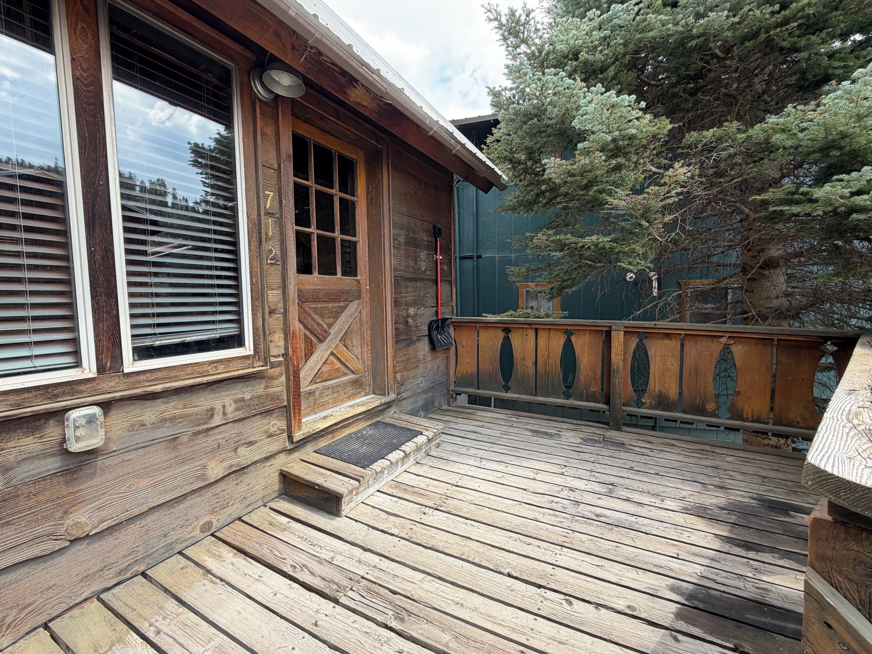 Eine Holzterrasse mit Holztür und -fenstern, einer kleinen Veranda und Blick auf einen Baum.