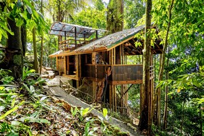A rustic wooden structure with a sloped roof, surrounded by dense forest. - Toucan's Nest Treehouse. Sleep in the canopy where rainforest meets the Ocean (Savegre de Aguirre, Puntarenas Province)