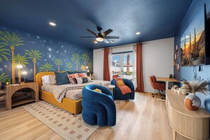 Een moderne slaapkamer met een bed, twee stoelen, een bureau en een plafondventilator.