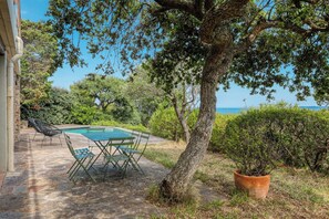 Un espace aménagé au bord de la piscine, avec une table et des chaises, entouré de verdure et offrant une vue sur la mer.