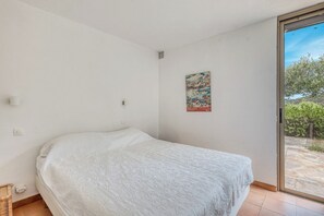 A bedroom with a bed, a window, and a door leading to an outdoor area. - Two-bedroom apartment with ocean views in Gaou Bénat—pool, private estate, beaches 5 minutes away (Bormes-les-Mimosas)