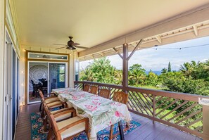 Un área de comedor al aire libre techada con una mesa preparada para dos, sillas de madera y vistas a follaje exuberante.