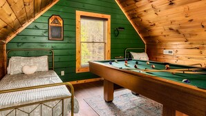 Quarto de sótão acolhedor com mesa de bilhar, cama com cabeceira e janela com persianas.