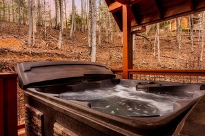 A hot tub with a wooden deck and a view of a forested area. - Quaint Cute Cabin|Pool Table|4min to Pkway|New|Hot Tub (Pigeon Forge)