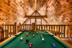 A pool table in a wooden room with a sloped ceiling and a view of trees outside. - Quaint Cute Cabin|Pool Table|4min to Pkway|New|Hot Tub (Pigeon Forge)