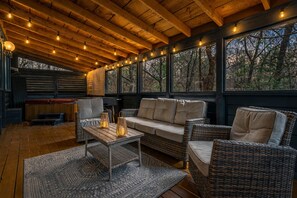 Un rincón exterior acogedor con mobiliario de mimbre, una mesa de madera y luces colgantes.