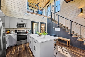 A modern kitchen with a central island, stainless steel appliances, and a wooden staircase leading to an upper level. - LUXE NEW! EZ Road, Hot Tub, Home Theater, Fire Pit (Sevierville)