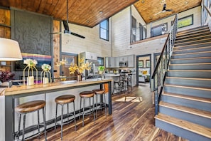 A spacious kitchen with a central island, bar stools, and a staircase leading to an upper level. - LUXE NEW! EZ Road, Hot Tub, Home Theater, Fire Pit (Sevierville)