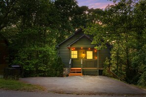 A small, green cabin with a porch, surrounded by dense trees. - Romantic Cabin w/ Hot Tub • 3mi to Pigeon Forge • King Bed • Fireplace (Pigeon For)