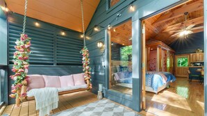 Una stanza accogliente con pavimento in legno, un letto con biancheria a motivi decorativi, un'elegante composizione floreale appesa e un'ampia finestra.