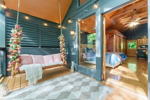 A cozy room with a wooden floor, a bed with patterned bedding, a hanging flower arrangement, and a large window. - Romantic Cabin w/ Hot Tub • 3mi to Pigeon Forge • King Bed • Fireplace (Pigeon For)