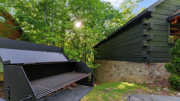 Una griglia da barbecue all'aperto, con un muro in pietra e un edificio in legno sullo sfondo.