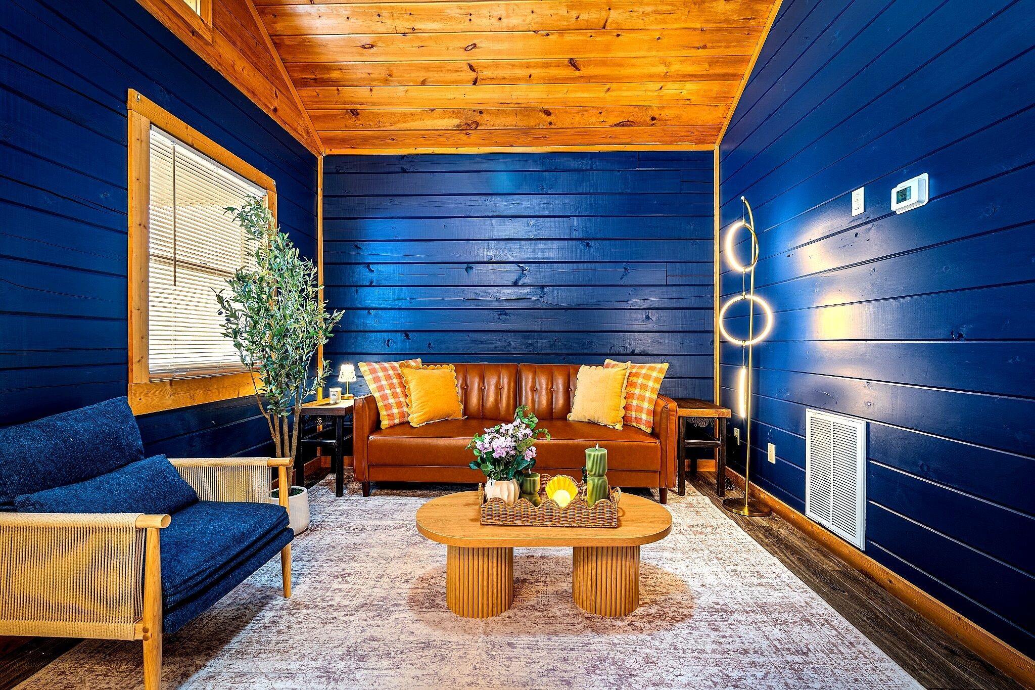 Ein gemütlicher Raum mit blauer Wand, braunem Sofa, blauem Sessel und Couchtisch mit Dekoration.
