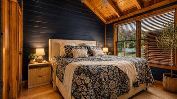 A bedroom with a large bed, wooden walls, a ceiling fan, and a window with blinds.