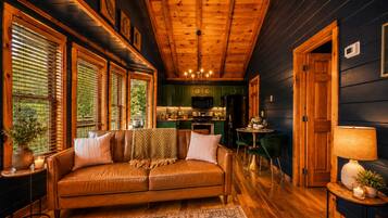 A cozy living room with a leather sofa, a dining area with a table and chairs, and a kitchen in the background.