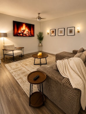 A living room with a sofa, a coffee table, a chair, a fireplace with a fire, a ceiling fan, and wall-mounted lights. - 2-bedroom apartment in lovely La Cantera Area with Pool View (San Antonio)
