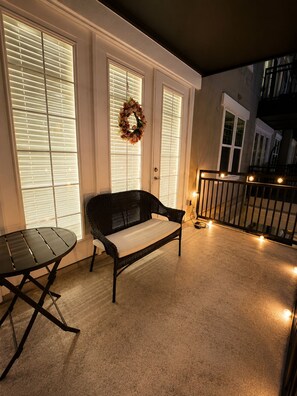 A balcony with a wicker sofa, a small table, and string lights. - 2-bedroom apartment in lovely La Cantera Area with Pool View (San Antonio)