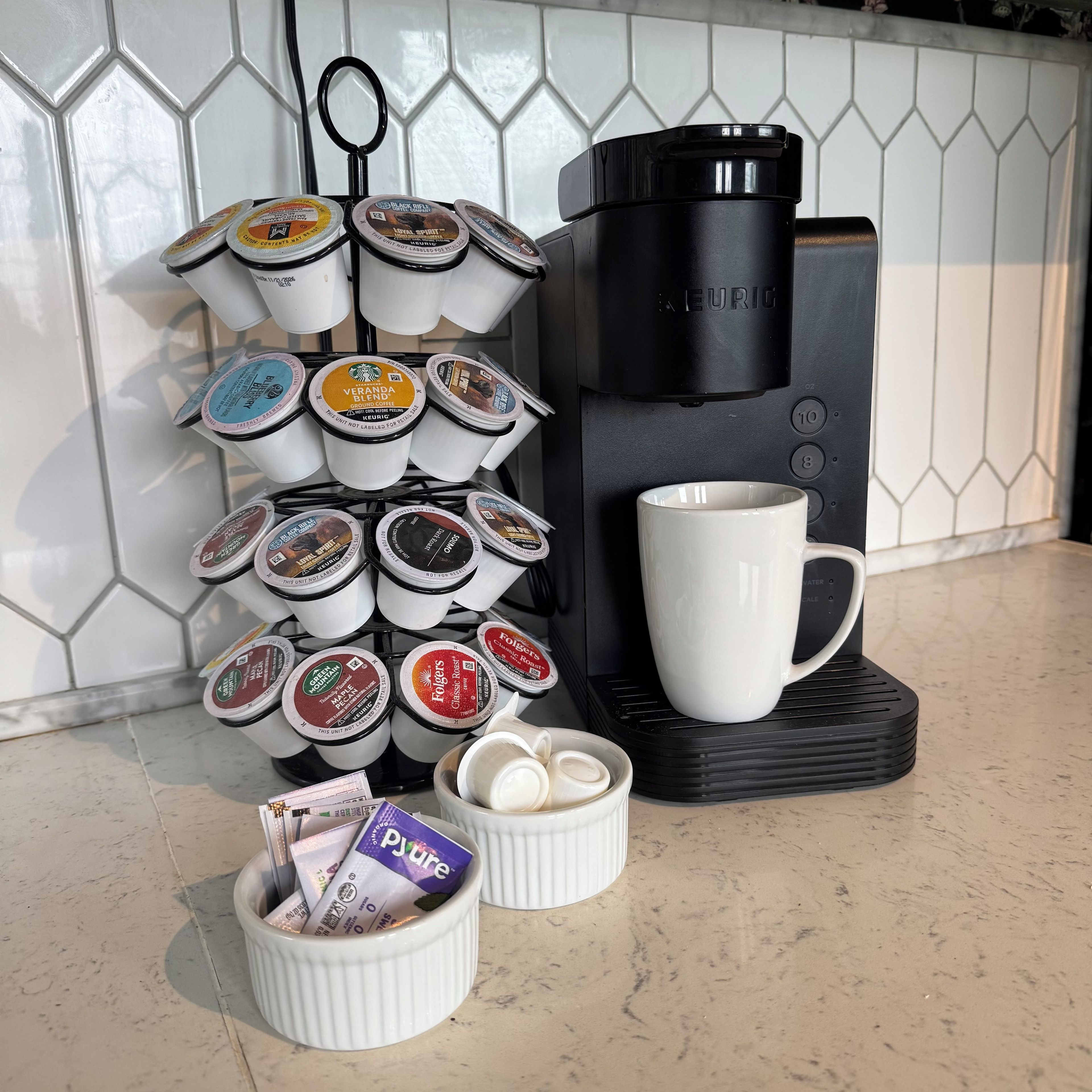 Una cafetera, una taza y varios pods de café sobre una encimera de cocina.
