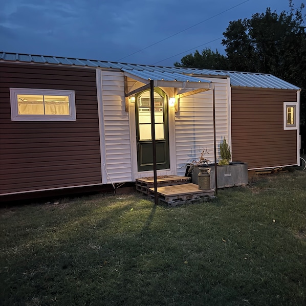 A single-story mobile home with a front porch, a small garden area, and a metal roof.