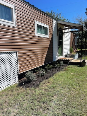 A single-story mobile home with a covered porch, a small window, and a fenced yard.