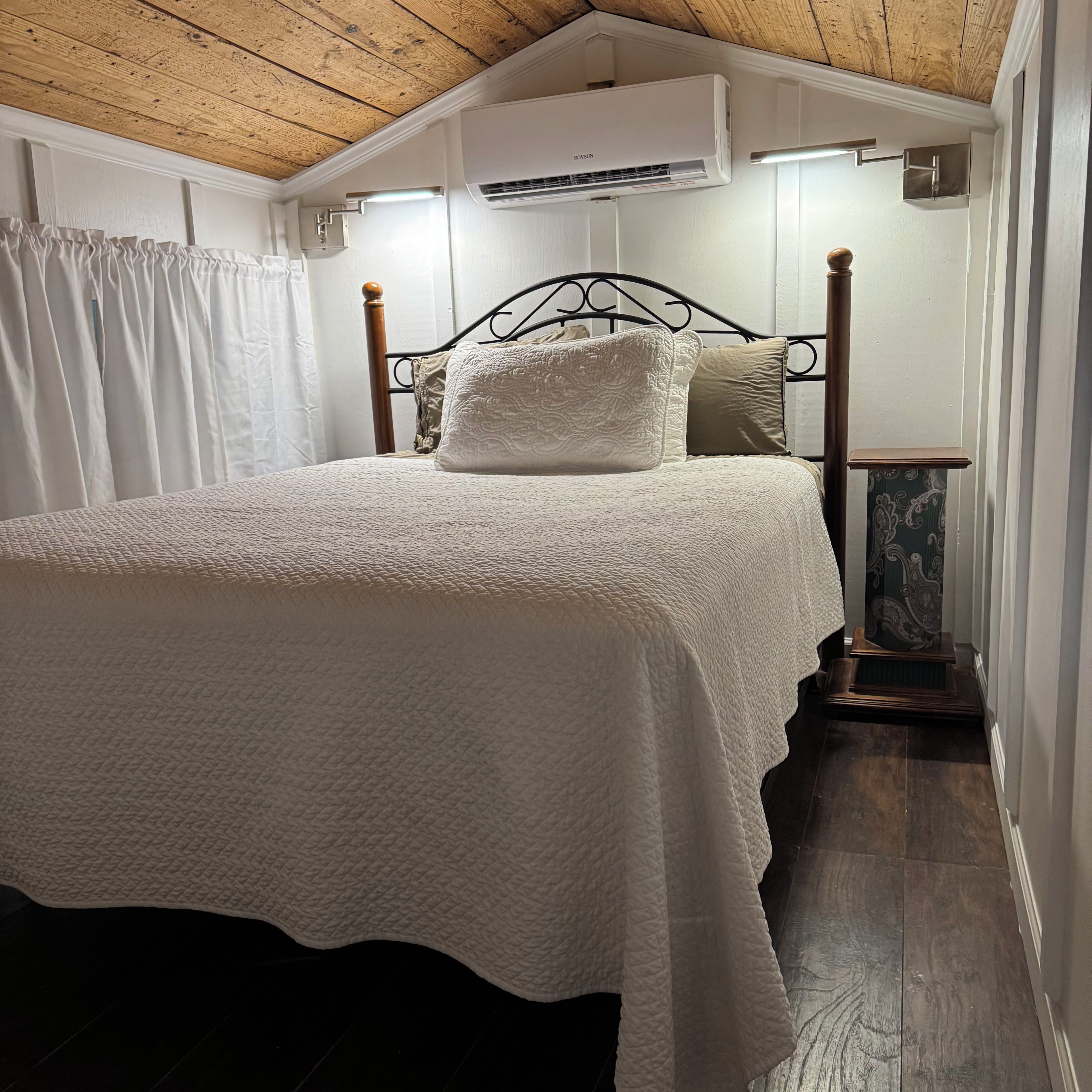Ein Schlafzimmer mit einem Bett, einem Holzkopfende, weißer Bettwäsche und einem Deckenventilator.